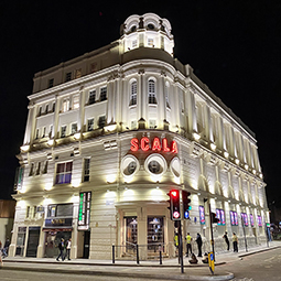 Four-floor building on the corner of two roads. Neon sign above entrance reads SCALA.
